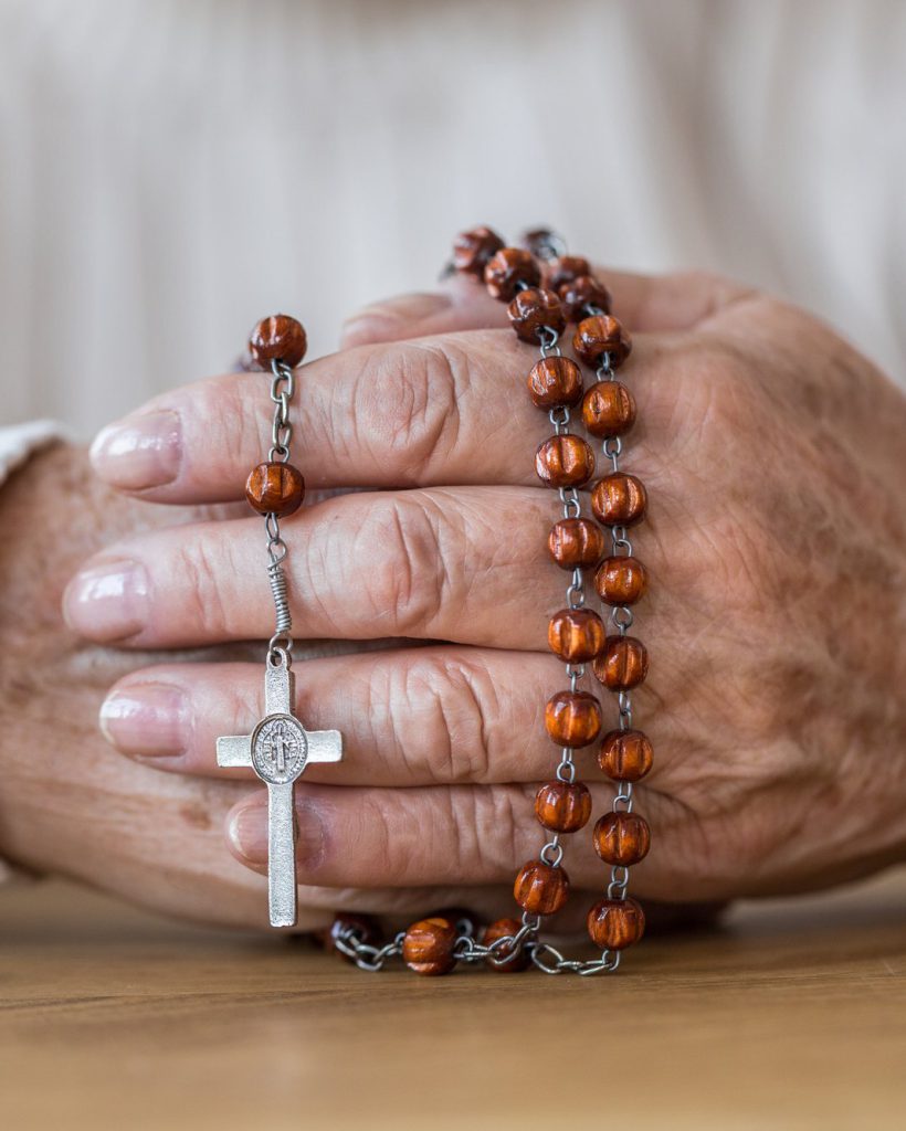 Close-up of senior's hands holding a red rosary with silver cross